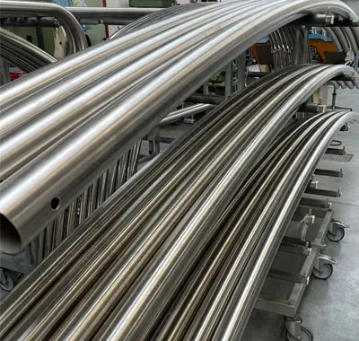 Gestapelte Metallrohre mit großem Radius, präzise gebogen und glänzend poliert, die auf einem Regal in einer Werkstatt gelagert sind.